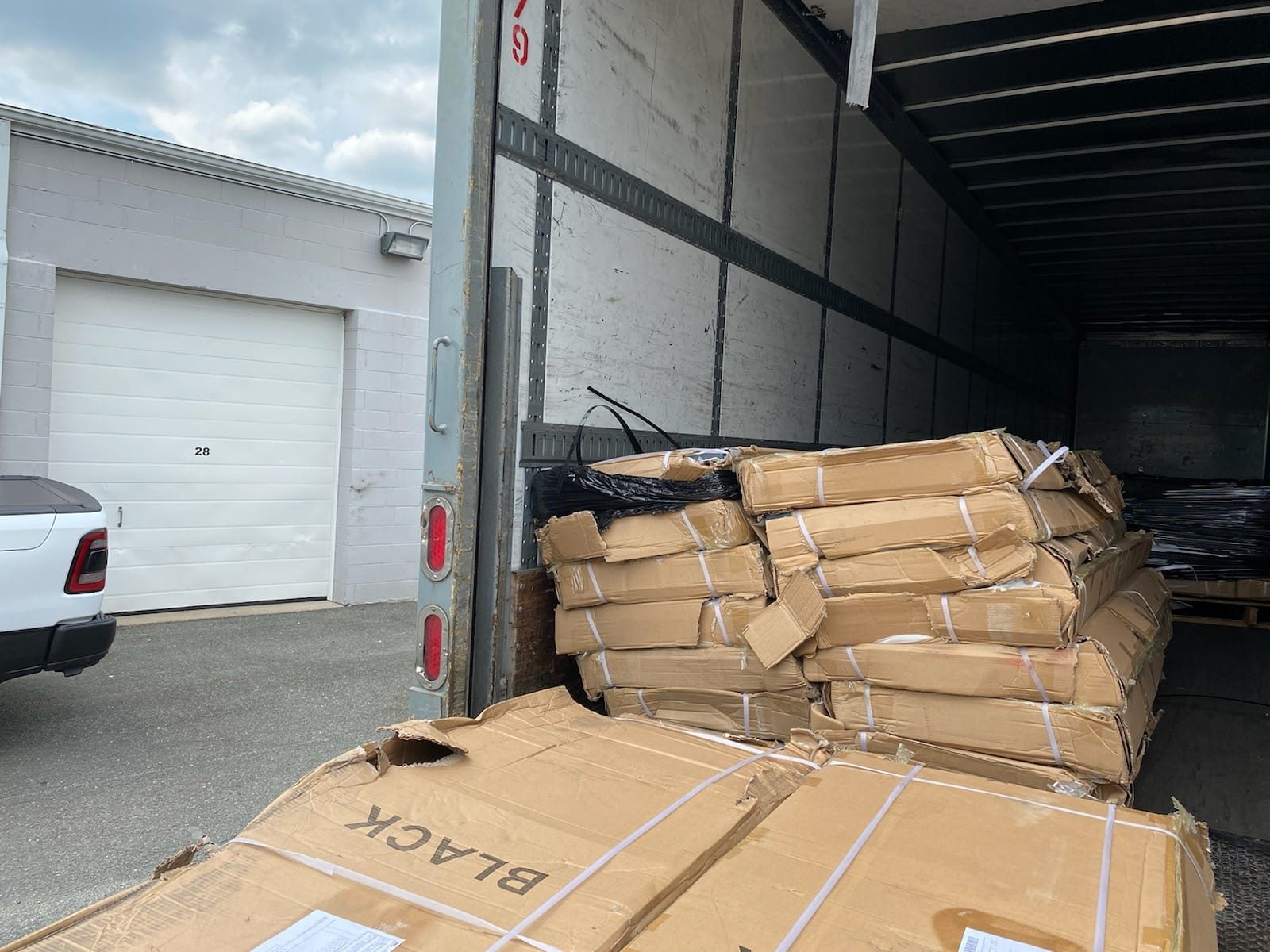 Damaged Breezy Laundry Lockers shipment in the back of a freight truck. Stacked cardboard cartons branded BLACK with torn corners, split seams, and visible internal contents at a US warehouse loading bay.