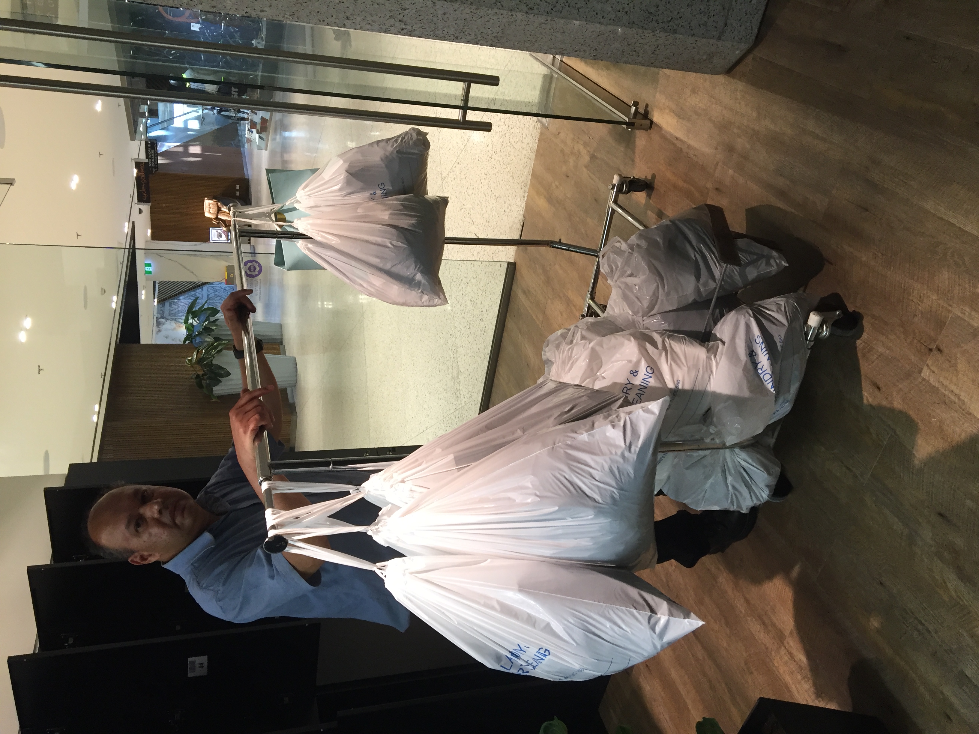 The operator pushing a rack stacked with finished laundry orders in white Breezy laundry bags through the mall corridor toward the locker store