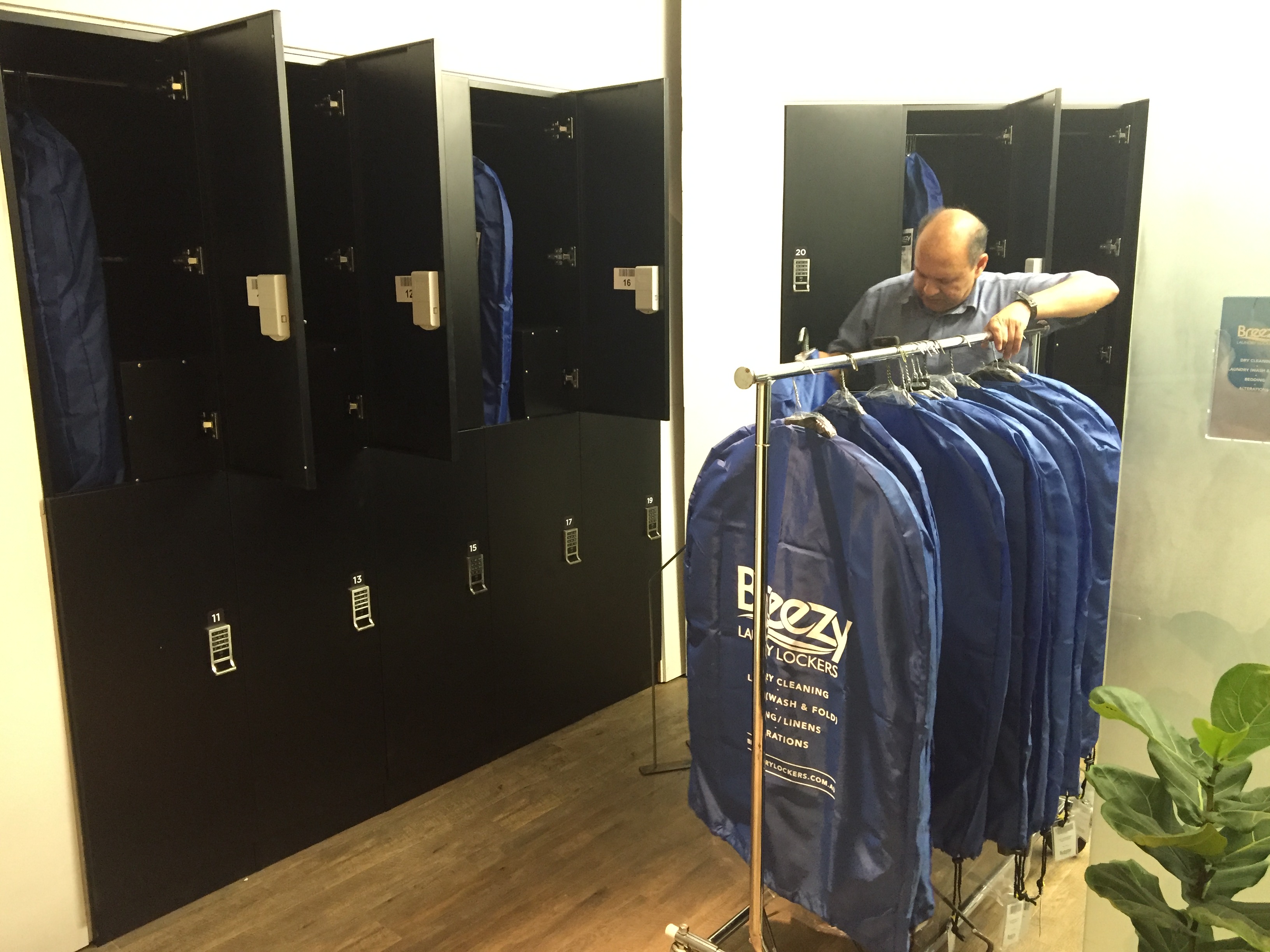 The owner restocking finished orders in branded blue Breezy garment bags on a rolling rack inside the operating store