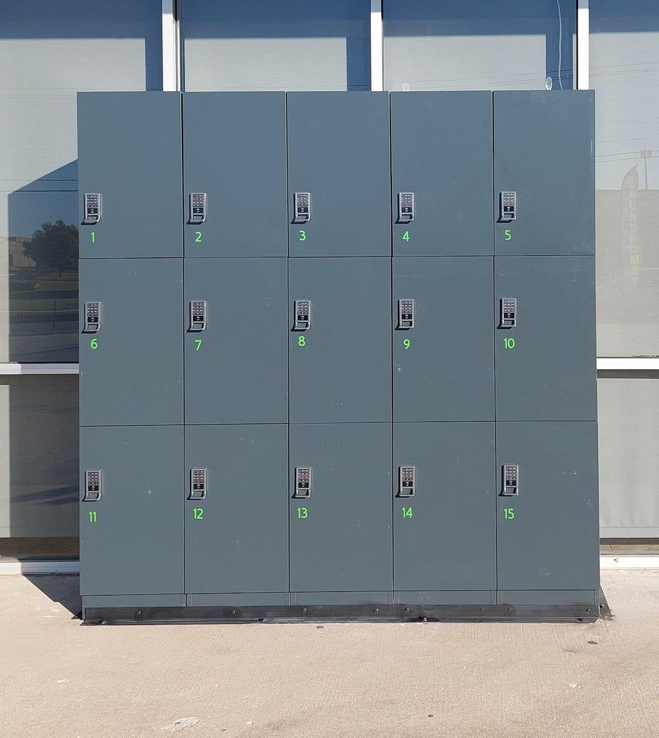 Bank of fifteen grey smart laundry lockers in a 5x3 arrangement at the exterior of a laundromat