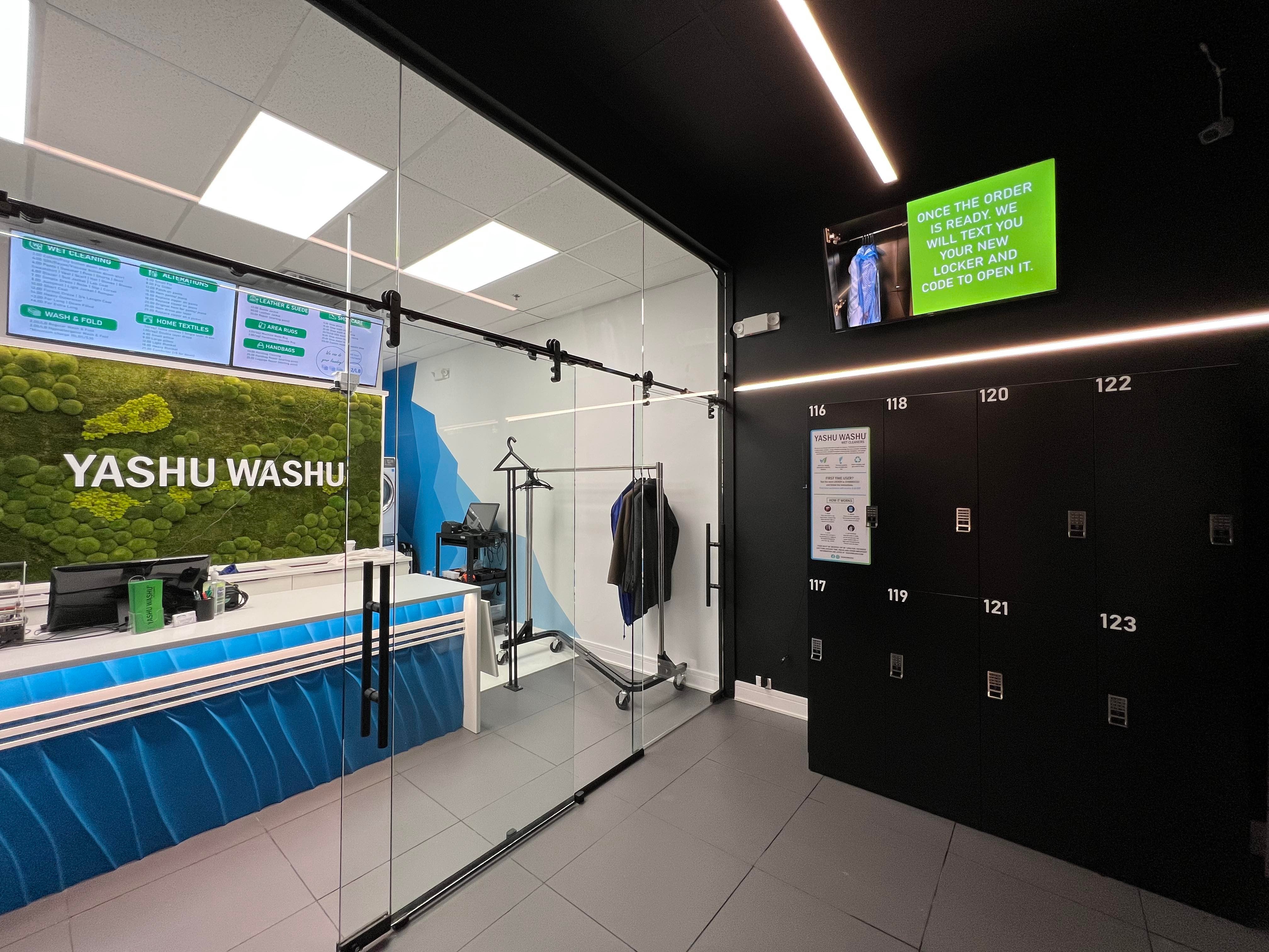 Interior of Yashu Washu retail laundry store showing a bank of black numbered smart laundry lockers along the wall with order-ready customer signage above — a real operating Breezy install